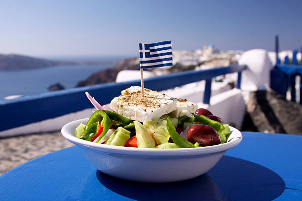 Greek salad served by the water in Santorini, Greece A perfect Greek salad, incorporating olives, green peppers and feta cheese, topped with a Greek flag, in Oia, Santorini greece stock pictures, royalty-free photos & images