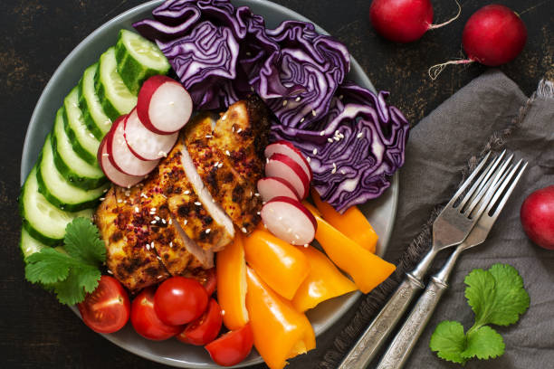 istock Fresh vegetables with baked chicken breast close up on rustic background,top view. Red cabbage, radish, sweet pepper, cilantro,cucumbers, tomatoes. 934678842