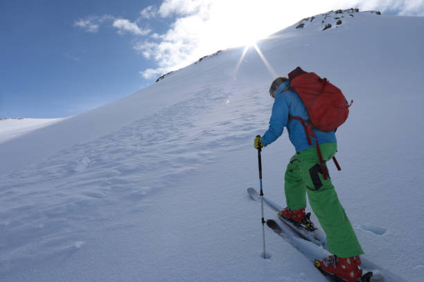 istock Ski mountaineer ascends slope towards mountain summit and sun. 934690990