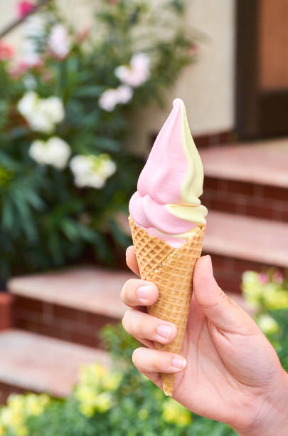 Hand of a young girl holding strawberry vanilla ice cream - with a blurred garden background