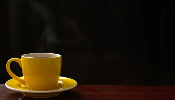 Yellow steam hot coffee cup on the wooden table place in front of the black background