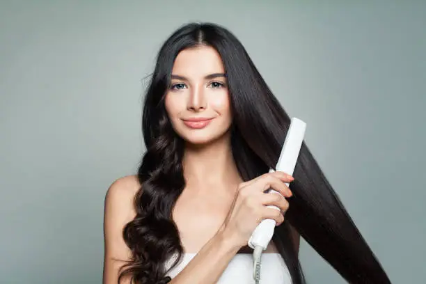 Photo of Attractive Woman with Curly Hair and Long Straight Hair Using Hair Straightener. Hair Problem and Haircare Concept