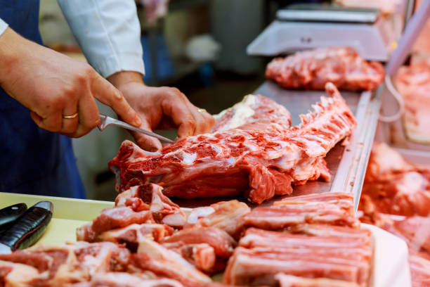 Cropped image of male butcher cutting raw meat with knife at counter shop Cropped image of male butcher cutting raw meat with knife at counter in shop meat packing industry photos stock pictures, royalty-free photos & images