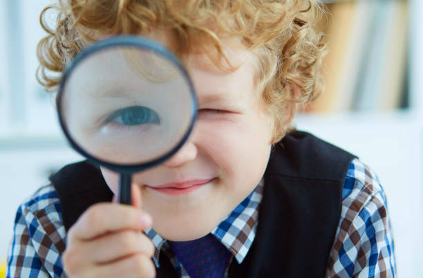 istock Little Caucasian boy looking at camera through magnifying glass in classroom. Studying the micro world with tools. 934764644