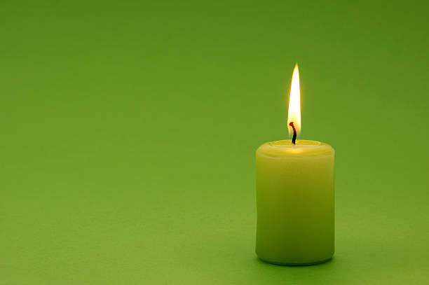 A lit green candle on a green background stock photo