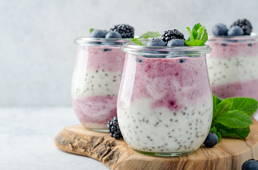 Acai berry and chia seed pudding with blueberries and blackberries in glass jars on a light white table. Copy space, horizontal image, front view