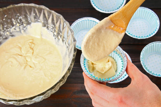 istock Hands pouring dough into molds for muffins on a wooden table. 934800048