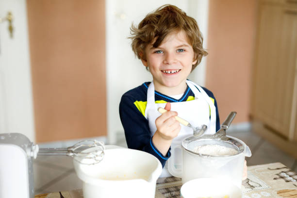 lindo engraçado loiro garoto garotinho fazendo bolo de chocolate e degustação de massa na cozinha doméstica - cake making mixing eggs - fotografias e filmes do acervo