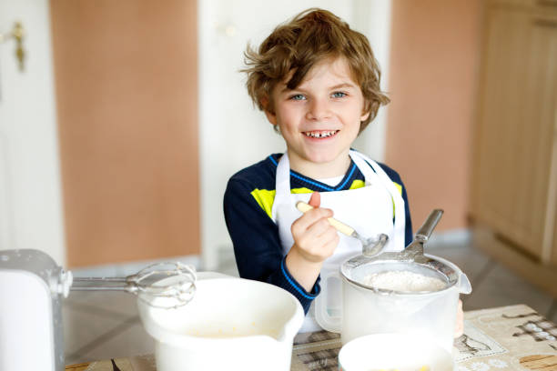 красивая смешная блондинка маленький мальчик выпечки шоколадный торт и дегустация теста в домашней кухне - cake making mixing eggs стоковые фото и изображения