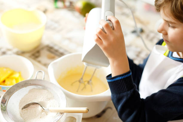 lindo engraçado loiro garoto garotinho fazendo bolo de chocolate e degustação de massa na cozinha doméstica - cake making mixing eggs - fotografias e filmes do acervo