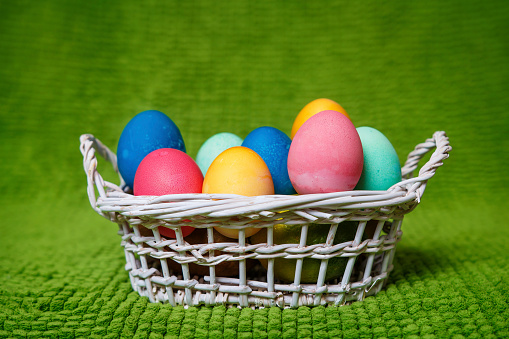Easter background. Multicolored easter eggs in a basket on a green background. Spring Christian religious holiday of Easter.