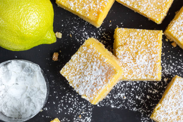 Lemon bars close up on black background ; Baked small lemon squares with whole lemon and powdered sugar