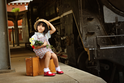 Little girl in straw hat sitting on her trunk and waiting for train