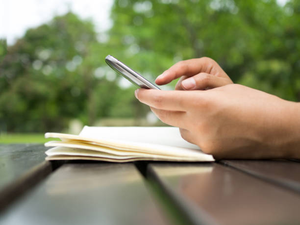 istock Woman hand holding phone and typing chatting on smartphone screen on table with notebook in natural park. 934850214