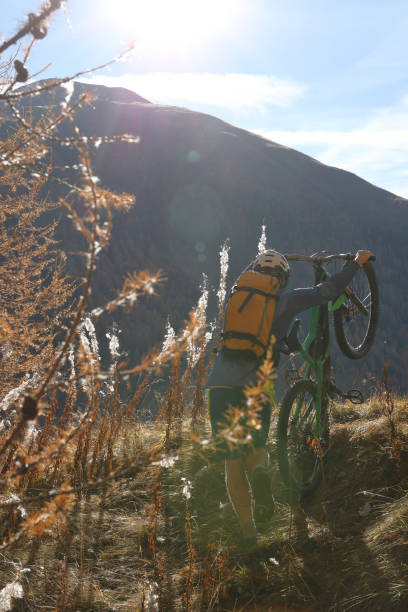 istock Young man pushes bike uphill in backlit grasses. 934855518