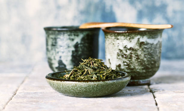 folhas de chá verde sencha e xícaras de chá de cerâmica japonesa - chá verde - fotografias e filmes do acervo