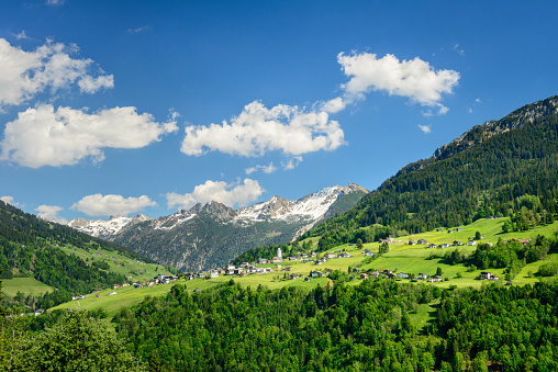 The idyllic mountain-village Marul in Vorarlberg in the Austrian alps. There is forest all around and a mountain-range with some white clouds and blue sky in the background.