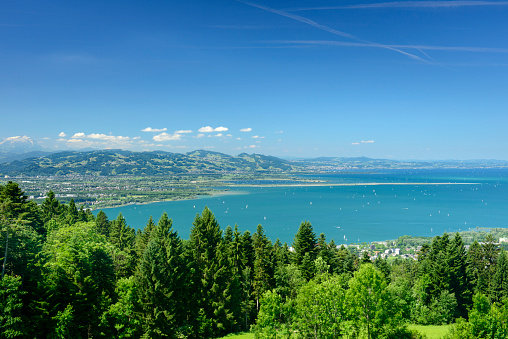 View from the idyllic mountain-village Eichenberg in Vorarlberg in the Austrian alps. There are hills with forest in the foreground and the lake of constance with the Swiss coast and mountains in the background.