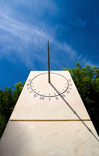Stone Sundial against a blue sky and some green tree tops.