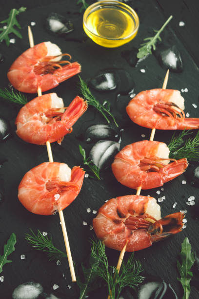 istock Grilled shrimp on a skewer with ice on dark backdrop. Top view 934921596