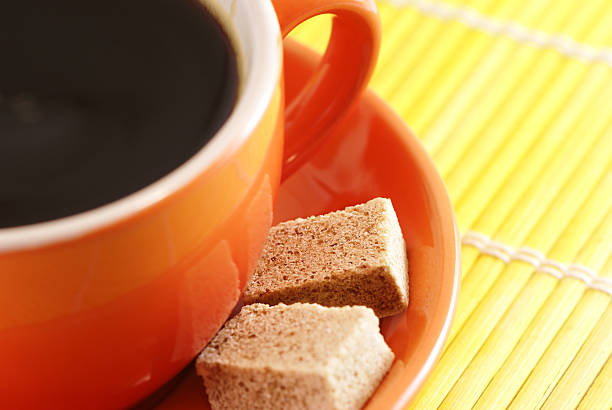 Demerara sugar falling from a silver teaspoon into a small cup of hot espresso coffee,in a domestic kitchen,Worcestershire,United Kingdom.