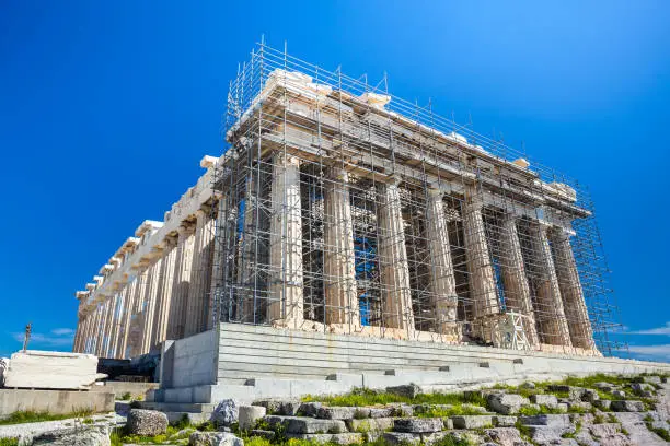 Photo of Restoration work in progress at world heritage ancient Parthenon with machine crane, scaffolding and blue sky background, Athens, Greece