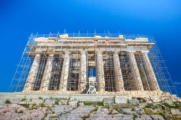 Photo of Restoration work in progress at world heritage ancient Parthenon with machine crane, scaffolding and blue sky background, Athens, Greece