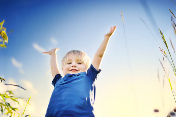 Cheerful little boy enjoying warm summer day. Active child playing in meadows. Freedom, rest and childhood concept. Happy kid outdoors