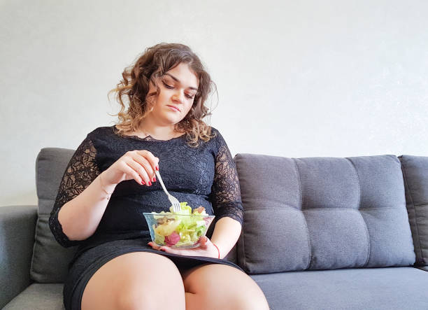 linda garota completo sentado no sofá com um prato de salada - overweight women salad frustration - fotografias e filmes do acervo