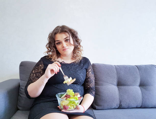 linda garota completo sentado no sofá com um prato de salada - overweight women salad frustration - fotografias e filmes do acervo