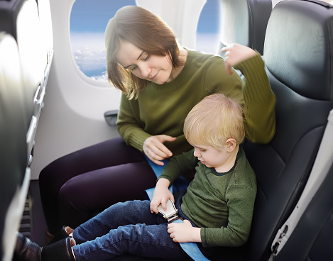 Young mother helping her little son with safety belt during traveling by an airplane. Traveling with kids. Family enjoying trip in aircraft. Transportation safety