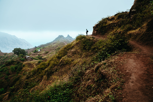 Hiker silhouette looks into the valley and listens to the silence. Fog and mist hang over the mountain peaks on the trail to Pompas. Santo Antao Cape Verde.