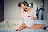 Shocked young girl with unwanted pregnancy looking the test in the bedroom