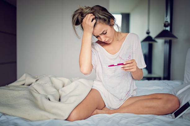 Shocked young girl with unwanted pregnancy looking the test in the bedroom stock photo