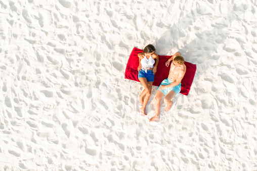 Top view of couple lying on white sand beach taking a sunbath in summer holiday