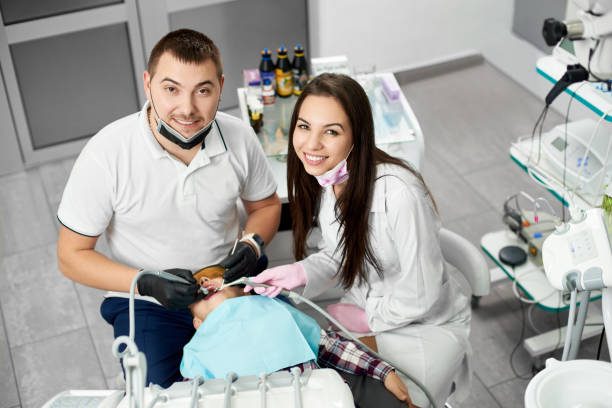 dentista masculina atraente e seu assistente feminina muito morena rae sorrindo para a câmera enquanto frequentava os dentes do seu cliente de criança. - medical exam dental hygiene caucasian mask - fotografias e filmes do acervo