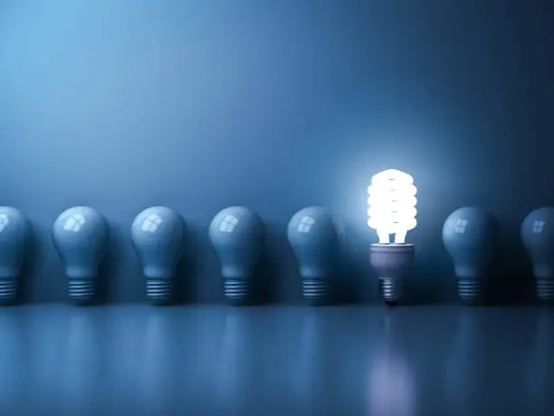 Eco energy saving light bulb , One glowing compact fluorescent lightbulb standing out from unlit incandescent bulbs reflection on blue background , individuality and different concept . 3D rendering.