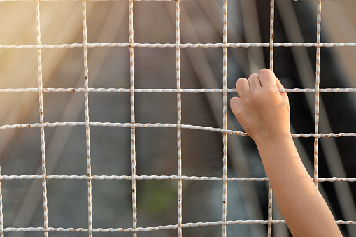 Children's hand with metal mesh cage or steel mesh fence.The concept of children's lack of independence.