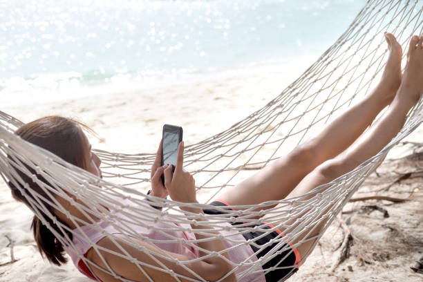 istock Woman using mobile phone on cozy mesh hammock at beach. 935205832