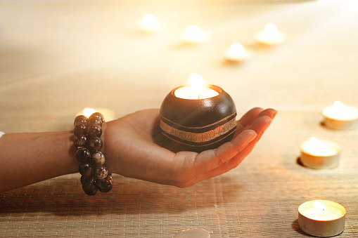 Woman hand yoga and meditation holding oil lamps in temple on candle warm glowing background