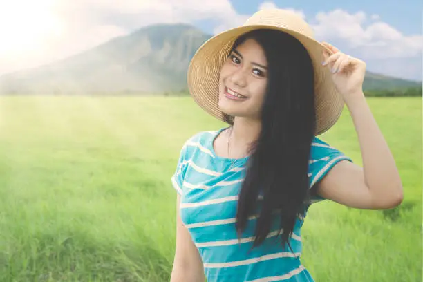 Beautiful woman wearing hat while standing on the meadow with mountain background