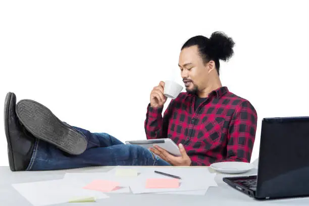 Happy professional worker drinking a cup of coffee and feet on desk isolated over white