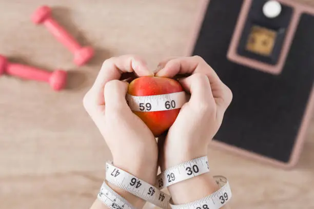 Photo of Woman's tied hands with a measuring tape and an apple. Heart shape. New start for healthy nutrition, body slimming, weight loss. Cares about body. Diet concept.