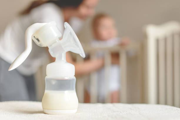 Manual breast pump and bottle with breast milk on the background of mother and baby near the baby's bed. Manual breast pump and bottle with breast milk on the background of mother and baby near the baby's bed. breast milk stock pictures, royalty-free photos & images