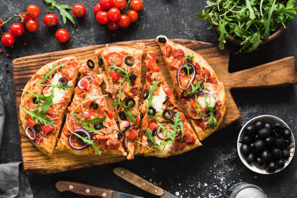 Flatbread pizza garnished with fresh arugula on wooden pizza board, top view Flatbread pizza garnished with fresh arugula on wooden pizza board, top view. Dark stone background flatbread stock pictures, royalty-free photos & images