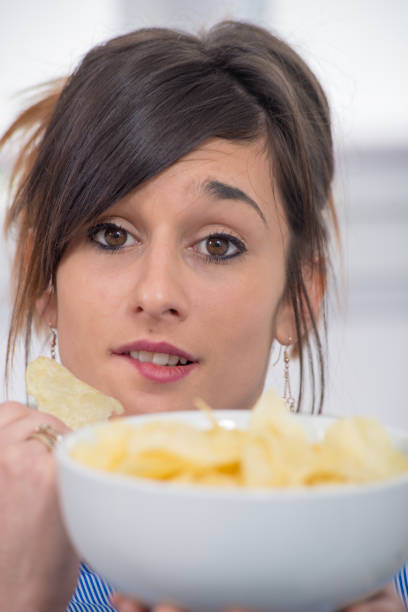 istock pretty young brunette woman eating chips 935297286