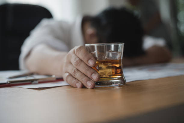 uomo d'affari asiatico stressato che tiene in mano un bicchiere di whisky che dorme e data charts, documento aziendale alla scrivania dell'ufficio.  dipendenza da alcol - concetto di uomo d'affari ubriaco - alcolismo foto e immagini stock