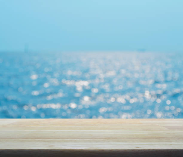 istock Empty wooden table with blur blue sea waves with bokeh light 935305532