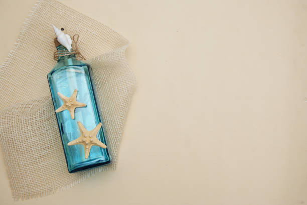 istock Nautical Theme Backdrop, Decorative Bottle with Shells, Starfish on Neutral Ivory Background. Place for text. Selective focus. 935317516