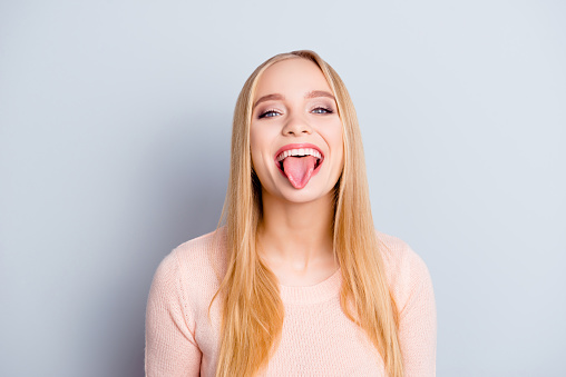 Close up portrait of funny childish playful careless carefree cheerful excited joyful beautiful delightful with long blond straight hairdo woman demonstrating tongue isolated on gray background